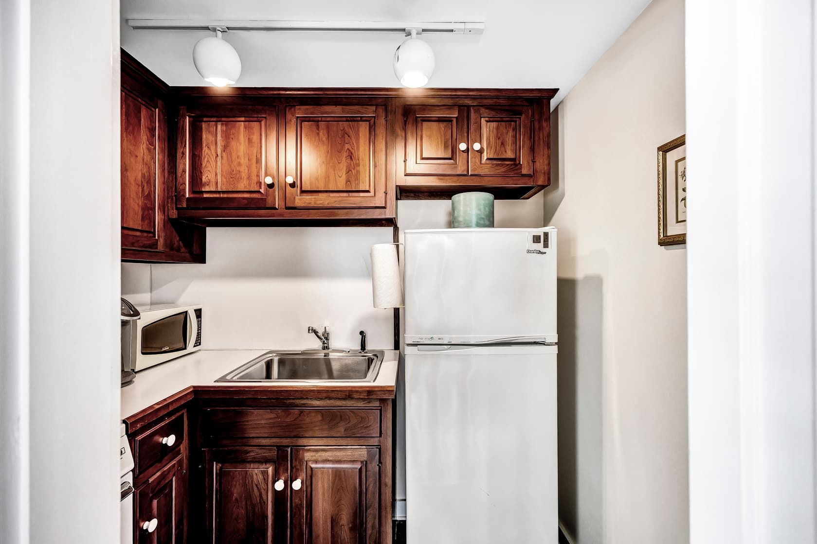 A bright bedroom with hardwood floors. There is a wooden four-poster bed with a white comforter and a blue and white patterned blanket.