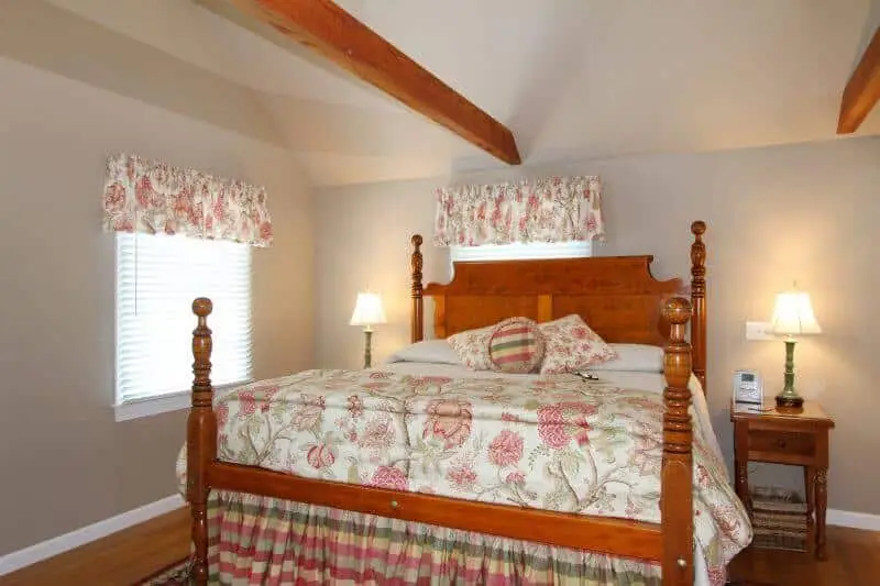 Four Poster King size bed with burgundy and green accented bedding, matching valances and exposed wooden beams, side tables with lamps shown