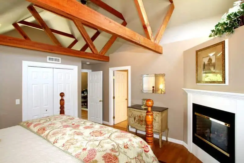 bedroom area with gas fireplace and shabby chic style painter dresser with mirror above, wooden floors, exposed wooden beams, white closest doors also shown