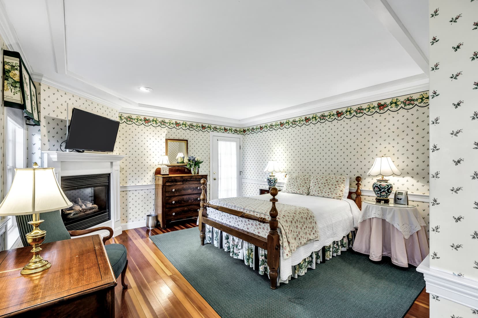 ADA compliant bathroom, pink walls with roses decor on top and middle, roll up sink, toilet with grab bars and shower with floral shower curtain, grab bars and hand held shower