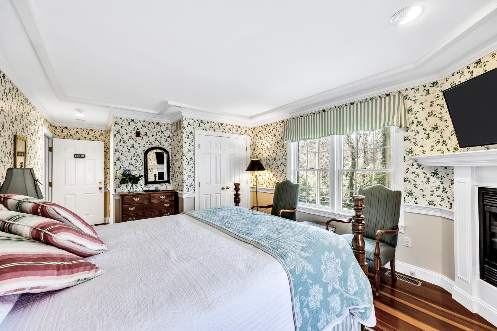 Queen bed, wallpaper pattern green ivy and red strawberries on white, fireplace, TV, door to patio area is open