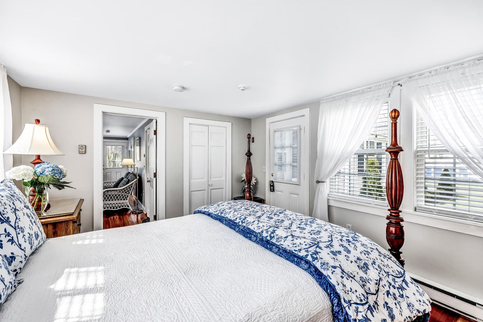 A bright living area with light blue walls and hardwood floors. There's a white wicker couch with a glass coffee table and a small kitchenette.