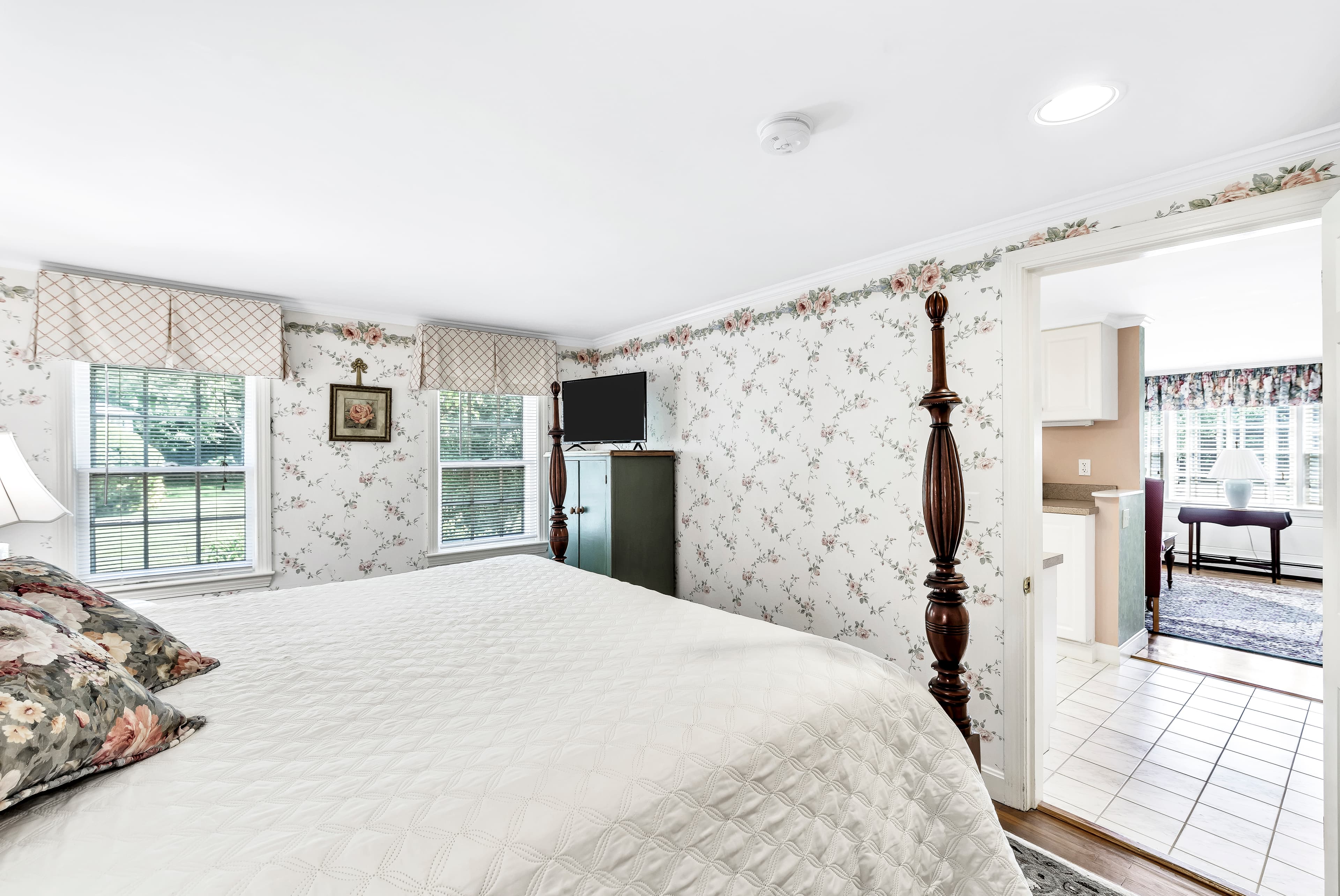 Large soaking tub surrounded with ceramic tile and pink roses wallpaper border to coordinate with the pale pink walls, vanity with sink and mirror above