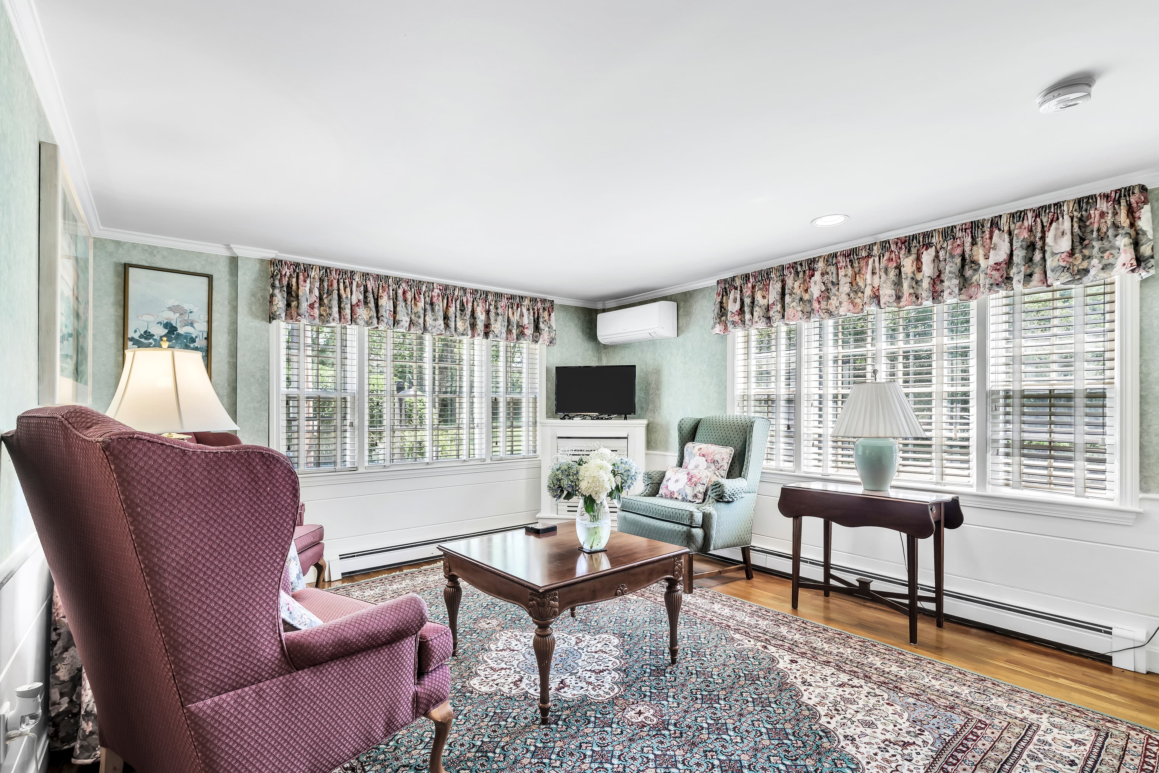 dusty pink bathroom walls, white pedestal sink with white wicker mirror above, toilet and floral picture above