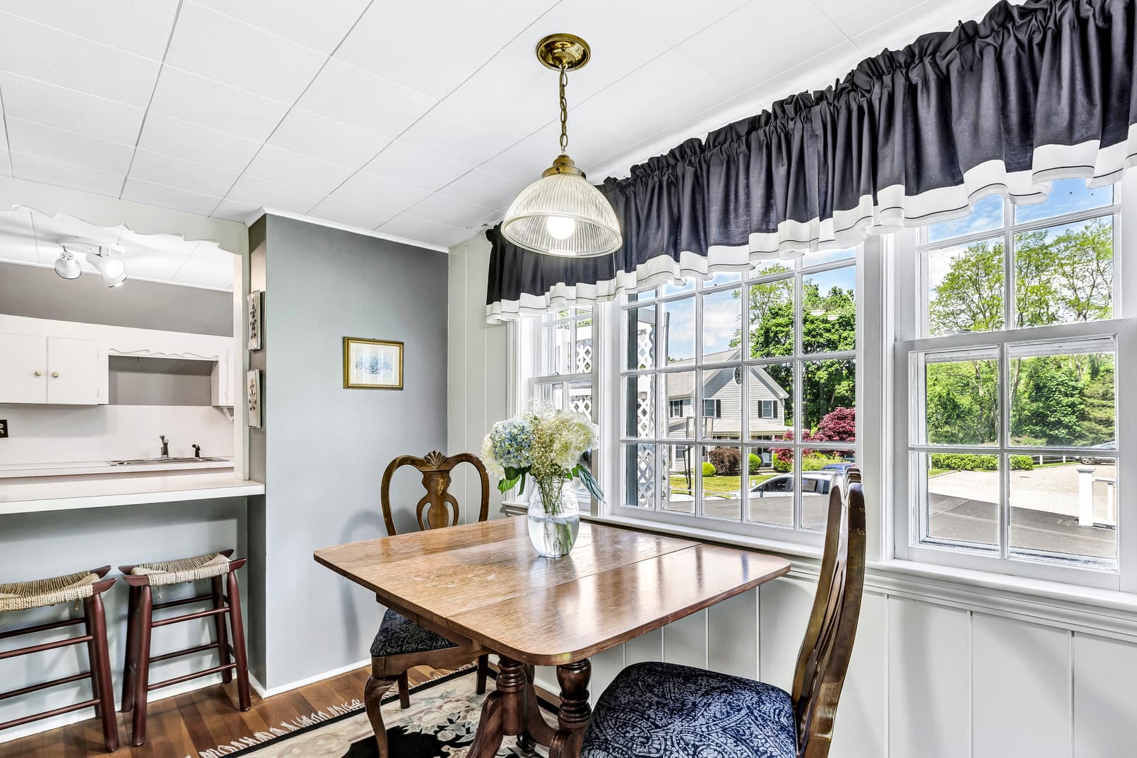 living room area with rattan reading chair, white sofa with navy decorative pillows, 2 brass scones above sofa, fireplace and wooden hutch