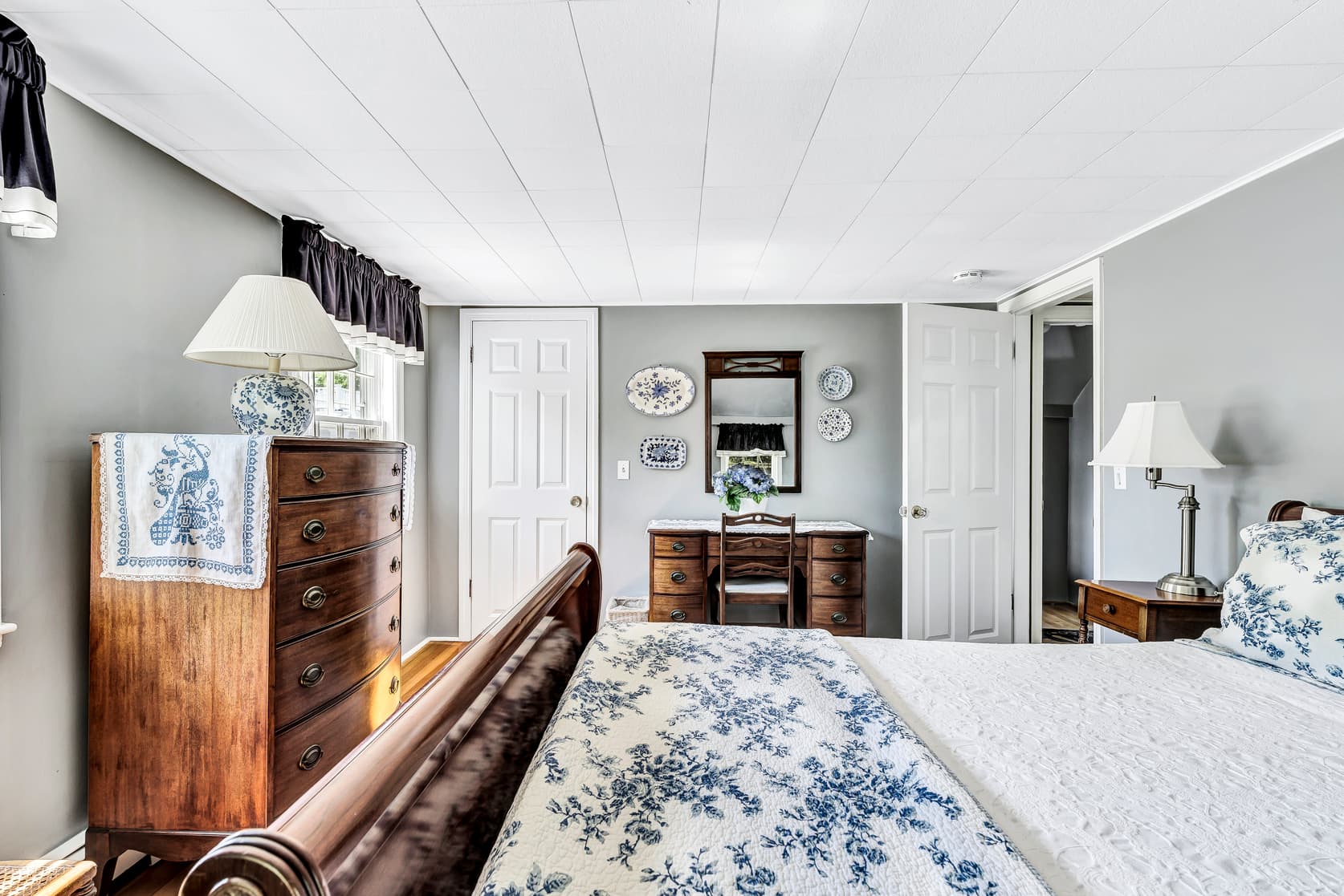view of dining area, wooden table with 2 chairs, windows that show view of the gardens on property, plant in corner, living room area with sofa, reading chair and fireplace, TV above fireplace