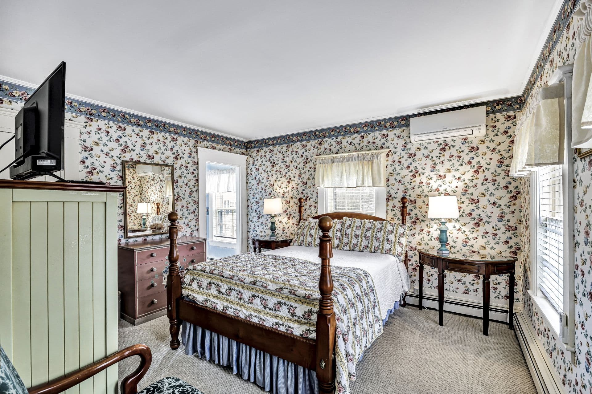 view of Queen bed with floral bed skirt and pink and white bedding, side tables and lamps, wooden dresser with mirror above
