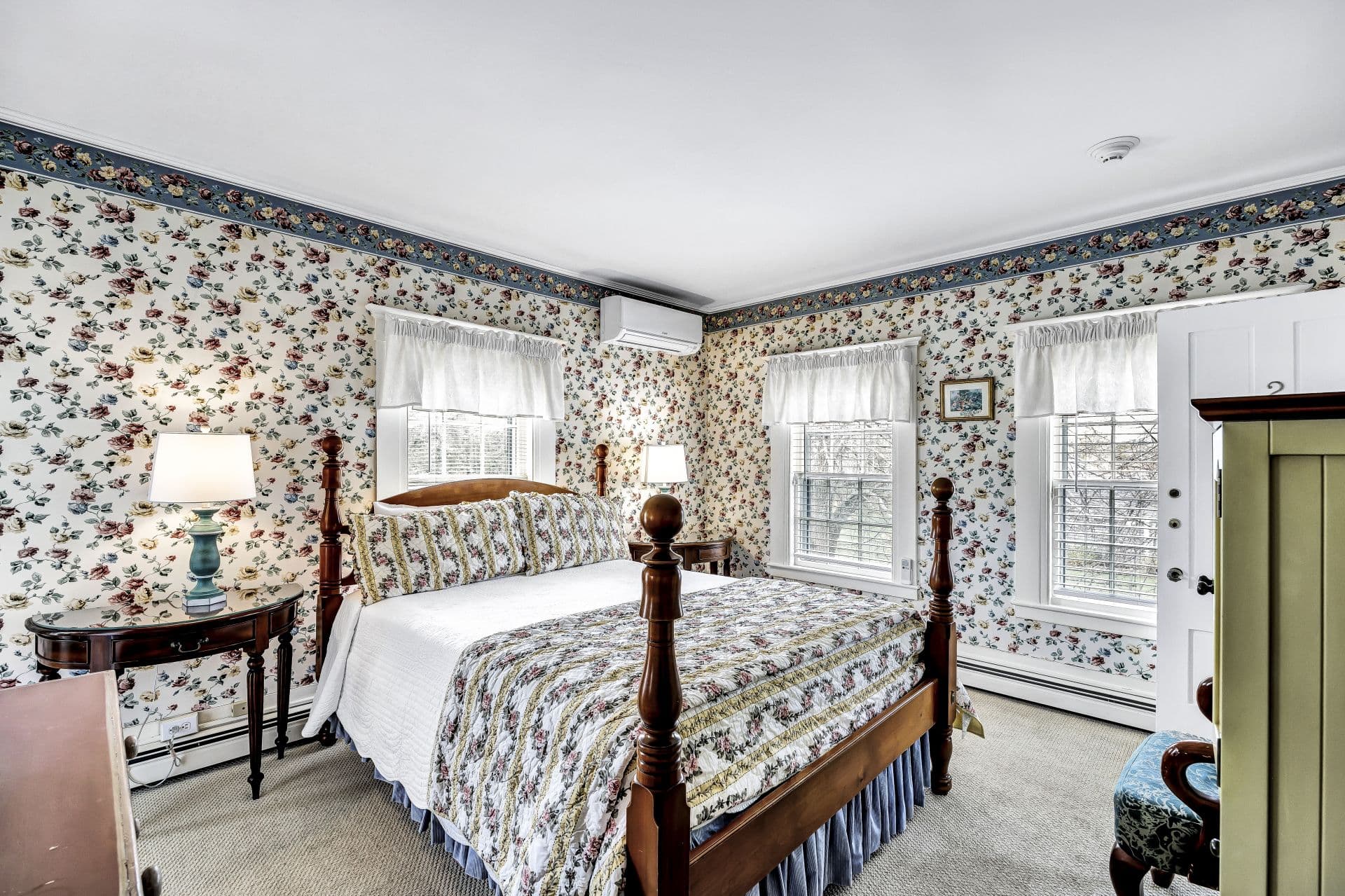 side view of Queen 4 poster bed with yellow stripes and roses bedding, white with yellow, pink and blue roses wall paper, dresser, side tables and lamps