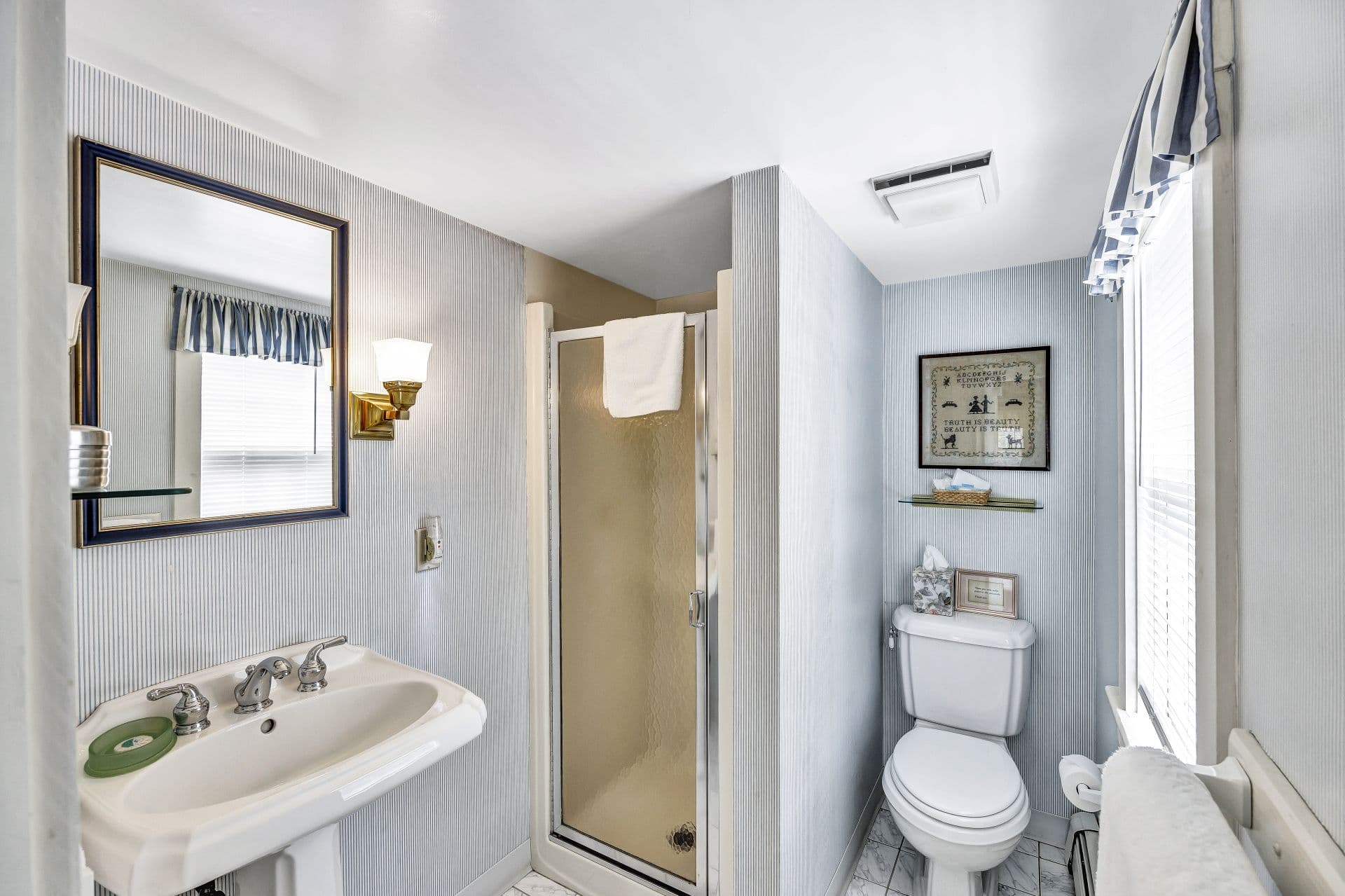 compact bathroom with shower, toilet and pedestal sink with mirror above