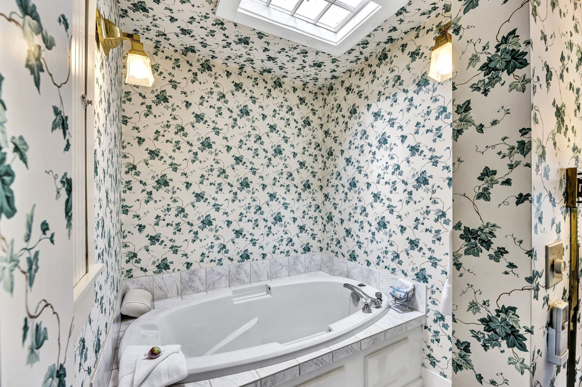 soaking tub under skylight surrounded by white with green ivy wallpaper