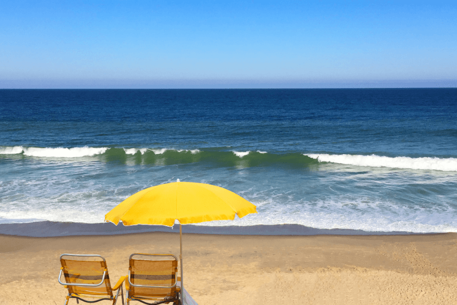 Two beach chairs under a yellow umbrella overlooking a calm ocean.