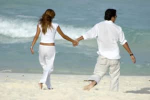 A couple walks hand-in-hand along a beach with gentle waves in the background. A couple walks hand-in-hand along a beach with gentle waves in the background.