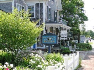 A charming shopfront with a grey wooden building, white picket fence, and vibrant flowers in the foreground.