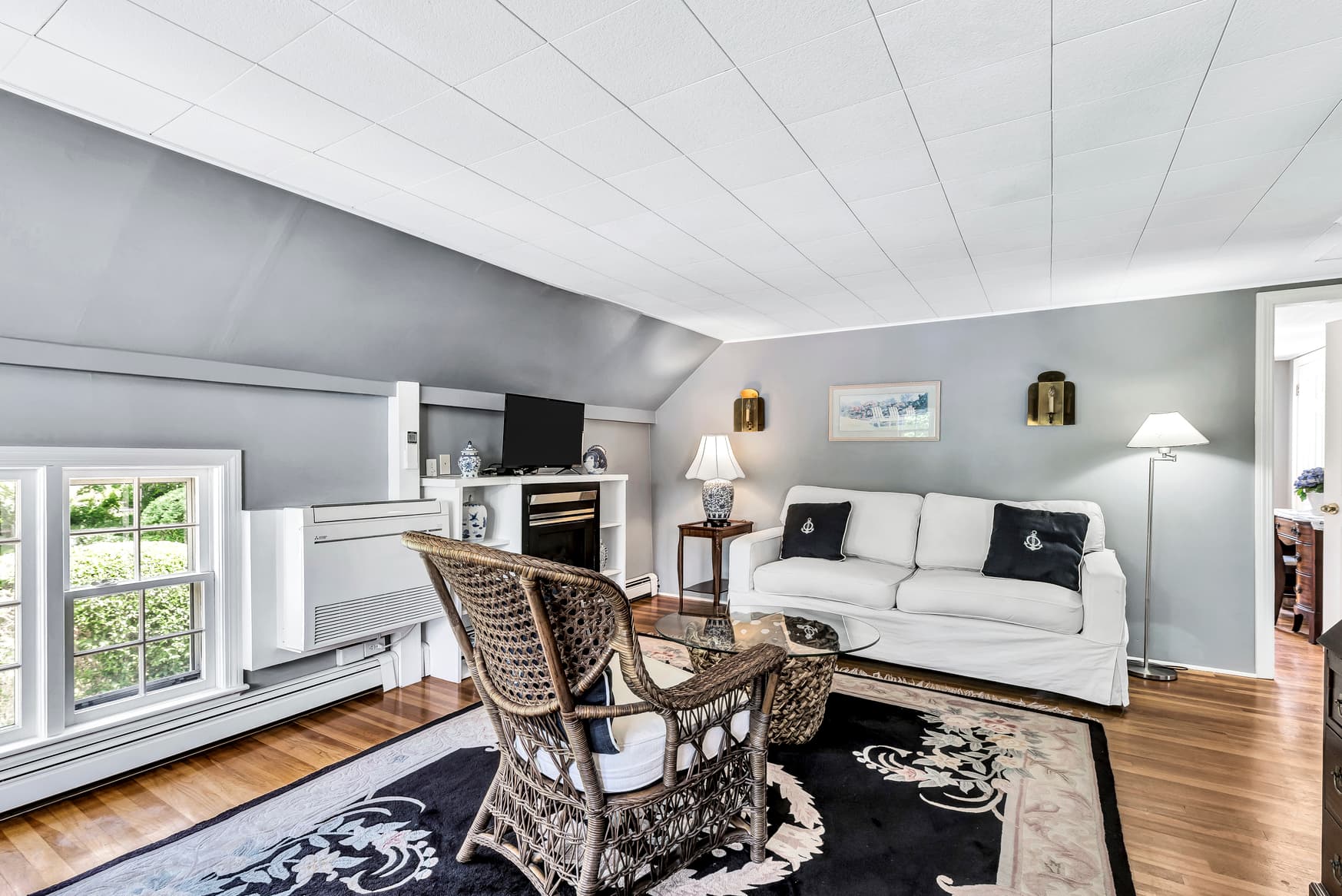 A cozy living room with a white sofa, a wicker chair, an area rug, and a fireplace against a gray wall.