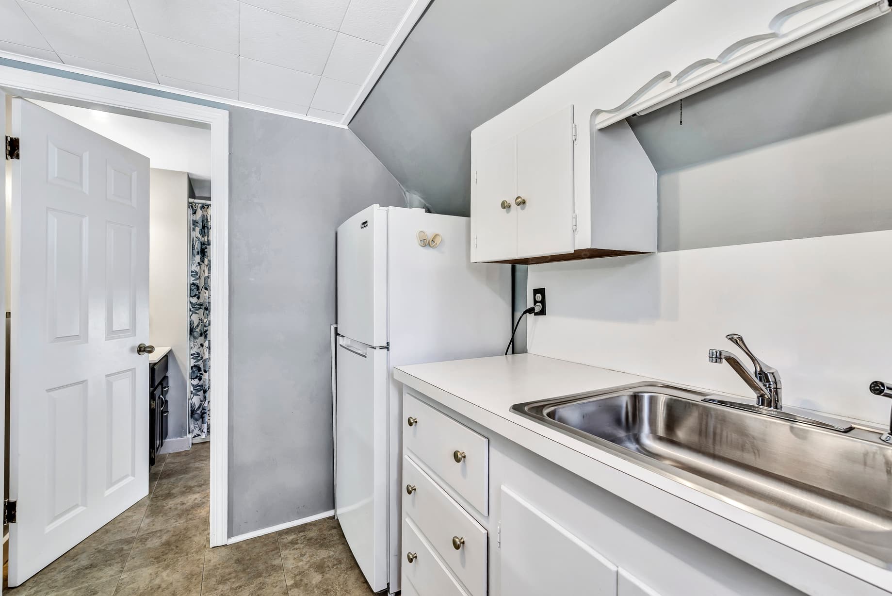 A compact kitchen featuring a sink, refrigerator, and simple cabinetry against a gray wall.