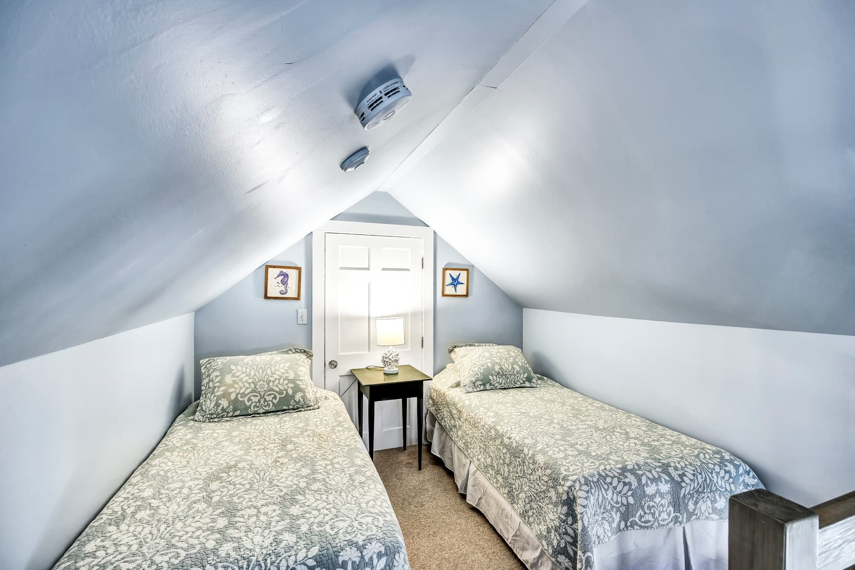 A cozy attic bedroom featuring two twin beds and light blue walls.