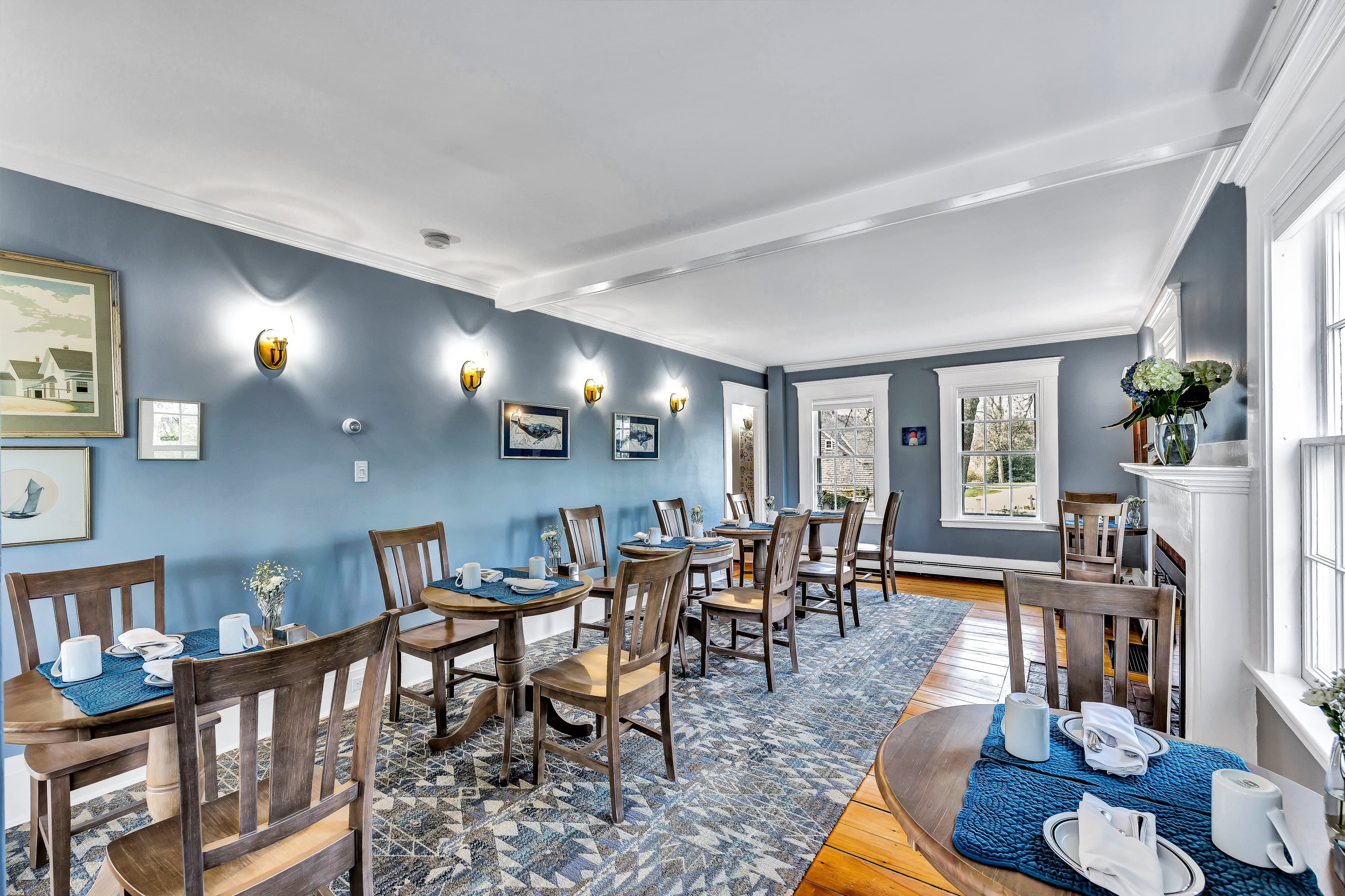 A bright dining area with wooden tables, blue walls, and large windows.