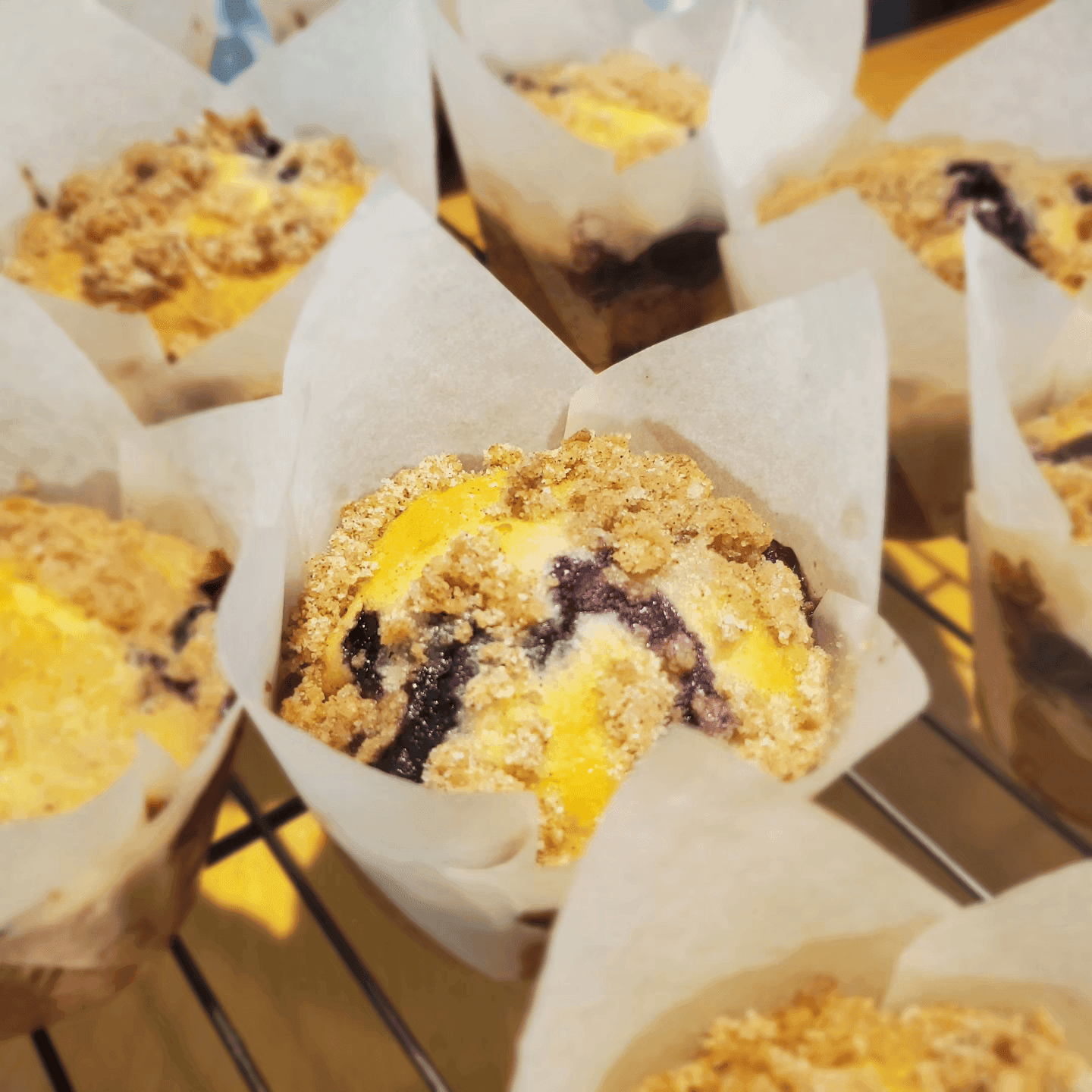 A close-up of freshly baked muffins with crumbly topping and a swirl of blueberries.