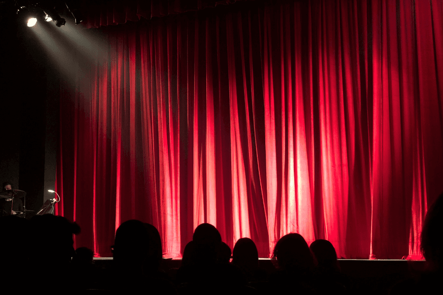 Theater scene with red curtains and an audience in silhouette.