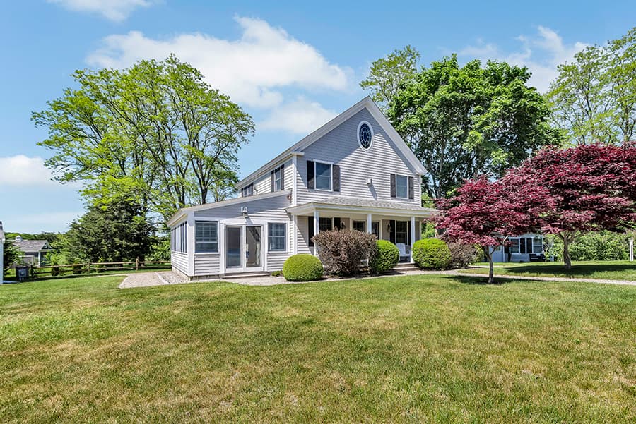 A two-story grey house surrounded by green lawns and trees.