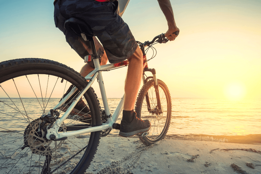 A person rides a mountain bike along the beach at sunset.