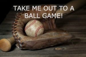 A baseball glove with a ball and a bat on a wooden surface, overlaid with the text "TAKE ME OUT TO A BALL GAME!"