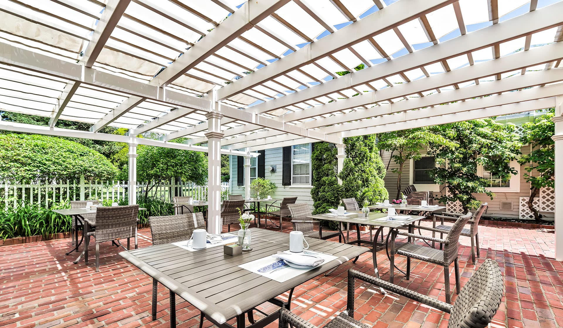 Outdoor dining area with tables under a pergola, surrounded by greenery.