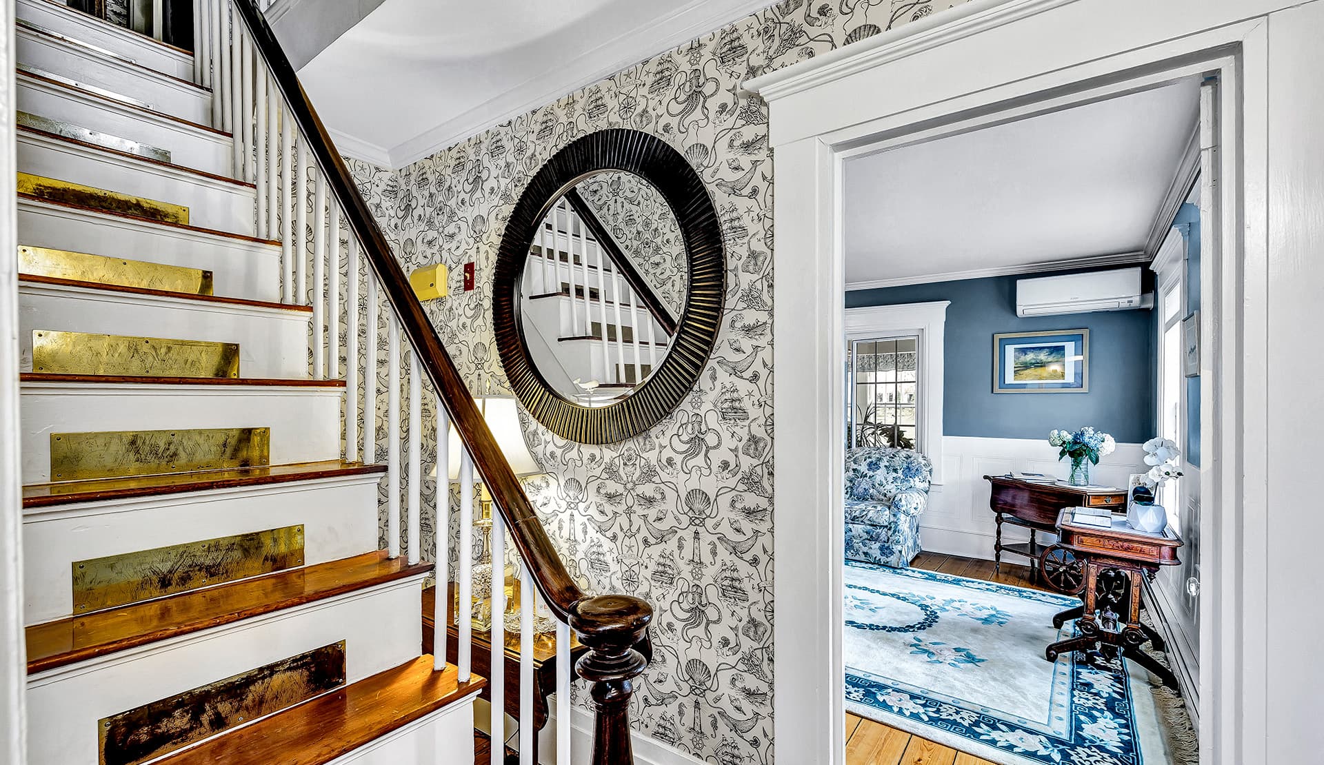 A staircase with brass inlays leads to a room featuring blue walls and patterned furniture.
