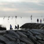 People walking along the rocky shore at dusk.