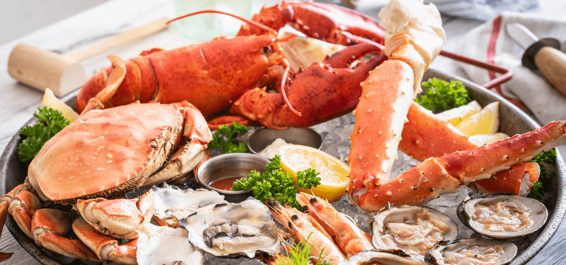 A plate of assorted seafood featuring lobster, crab, oysters, shrimp, and lemon wedges.