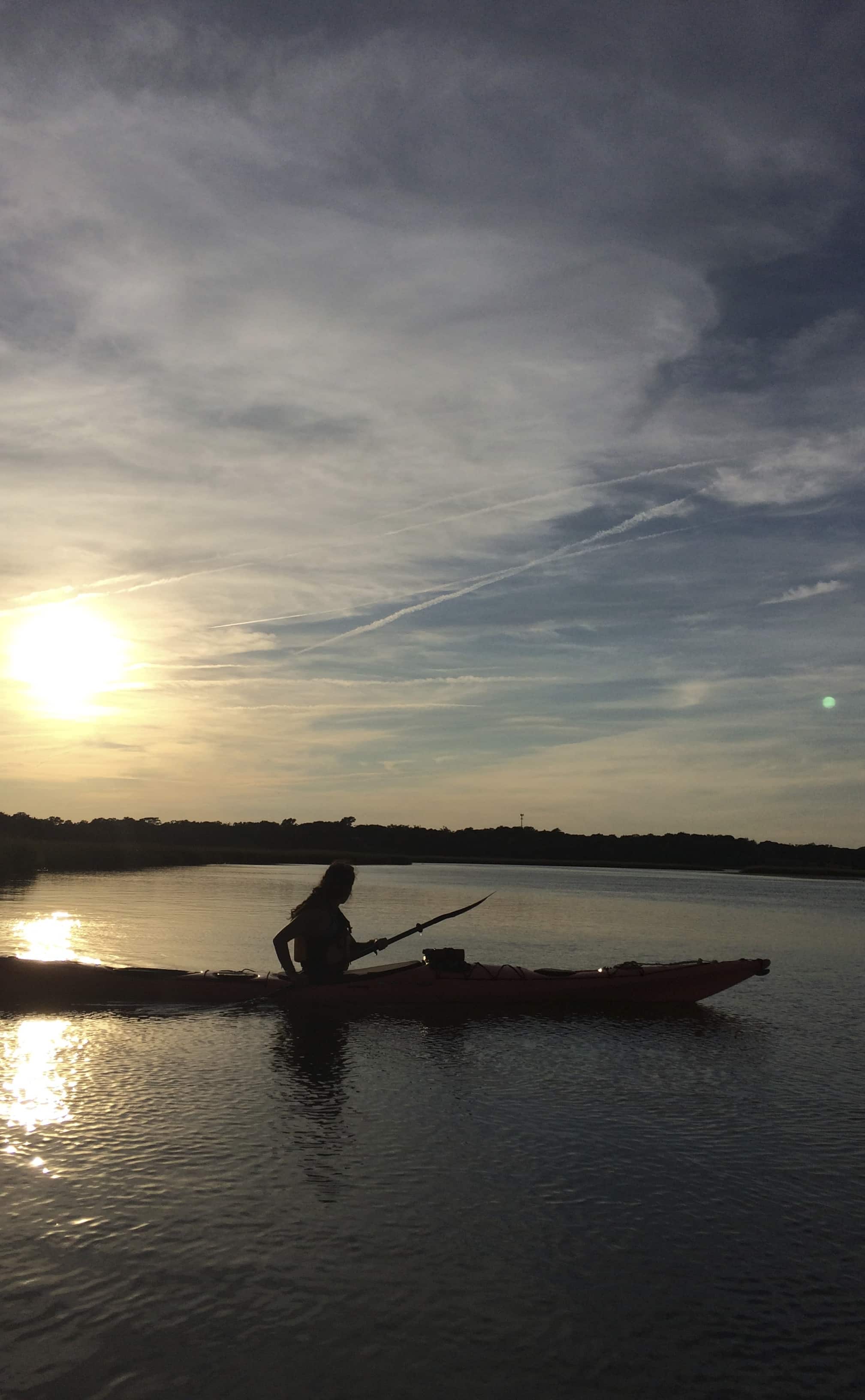 A silhouette of a person fishing from a kayak during sunset on a calm waterway. A silhouette of a person fishing from a kayak during sunset on a calm waterway.