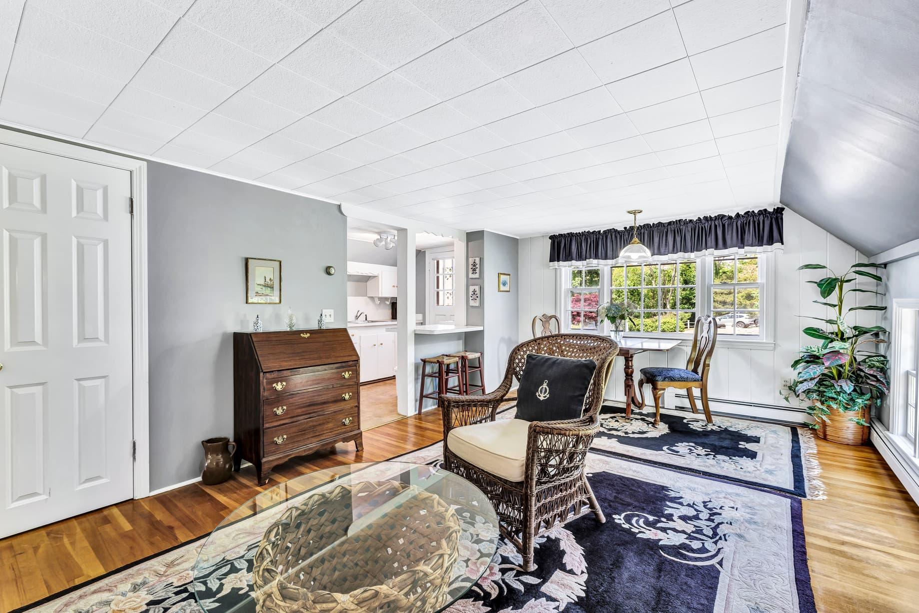 A cozy living room featuring a woven chair, wooden furniture, and natural light from a window.