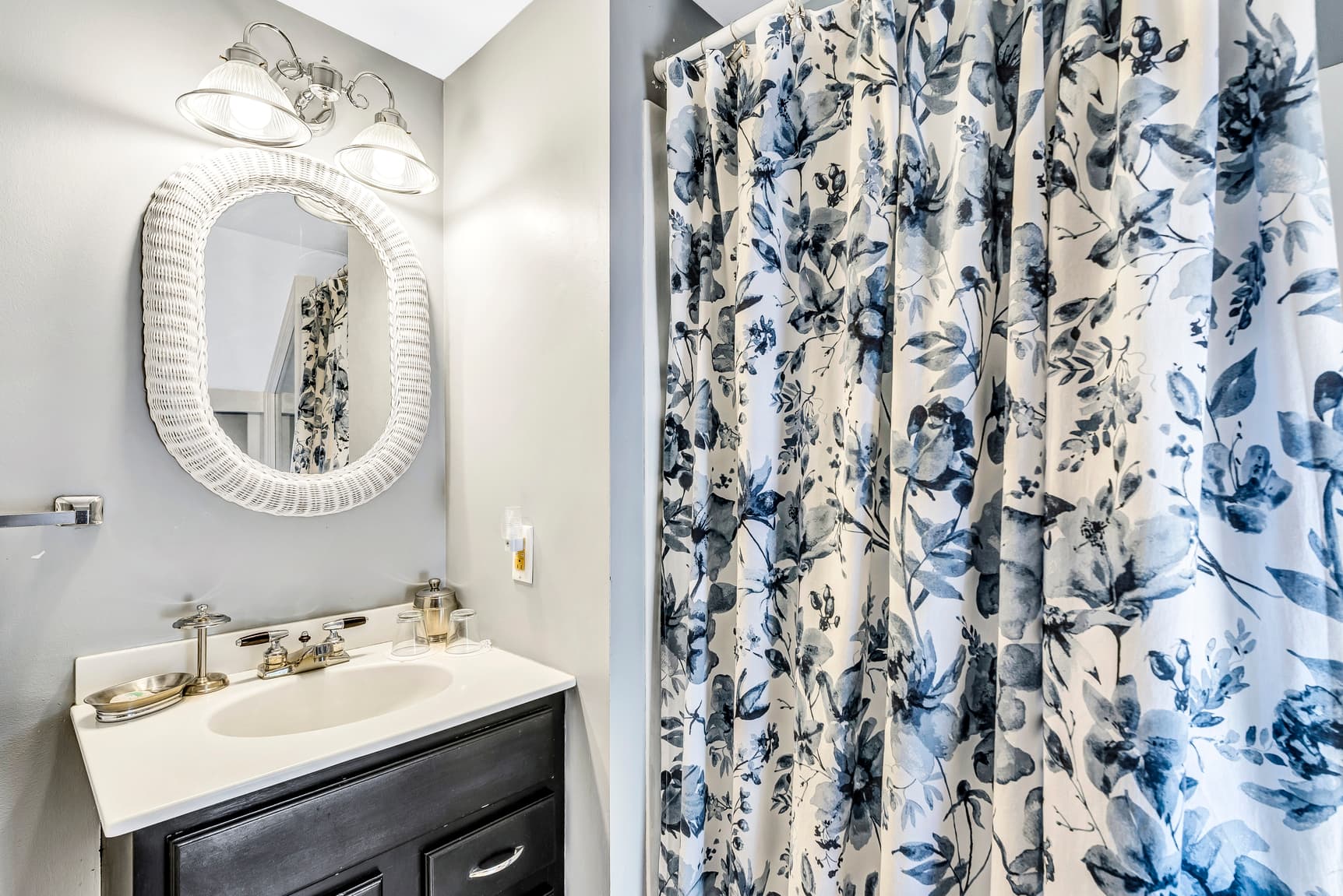 A modern bathroom featuring a dark vanity, a round mirror, decorative lighting, and a floral shower curtain.