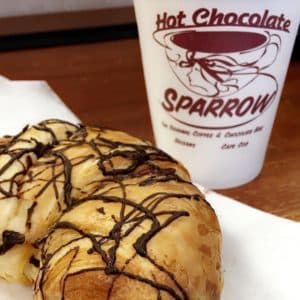 A chocolate-drizzled pastry next to a cup of hot chocolate from Sparrow.