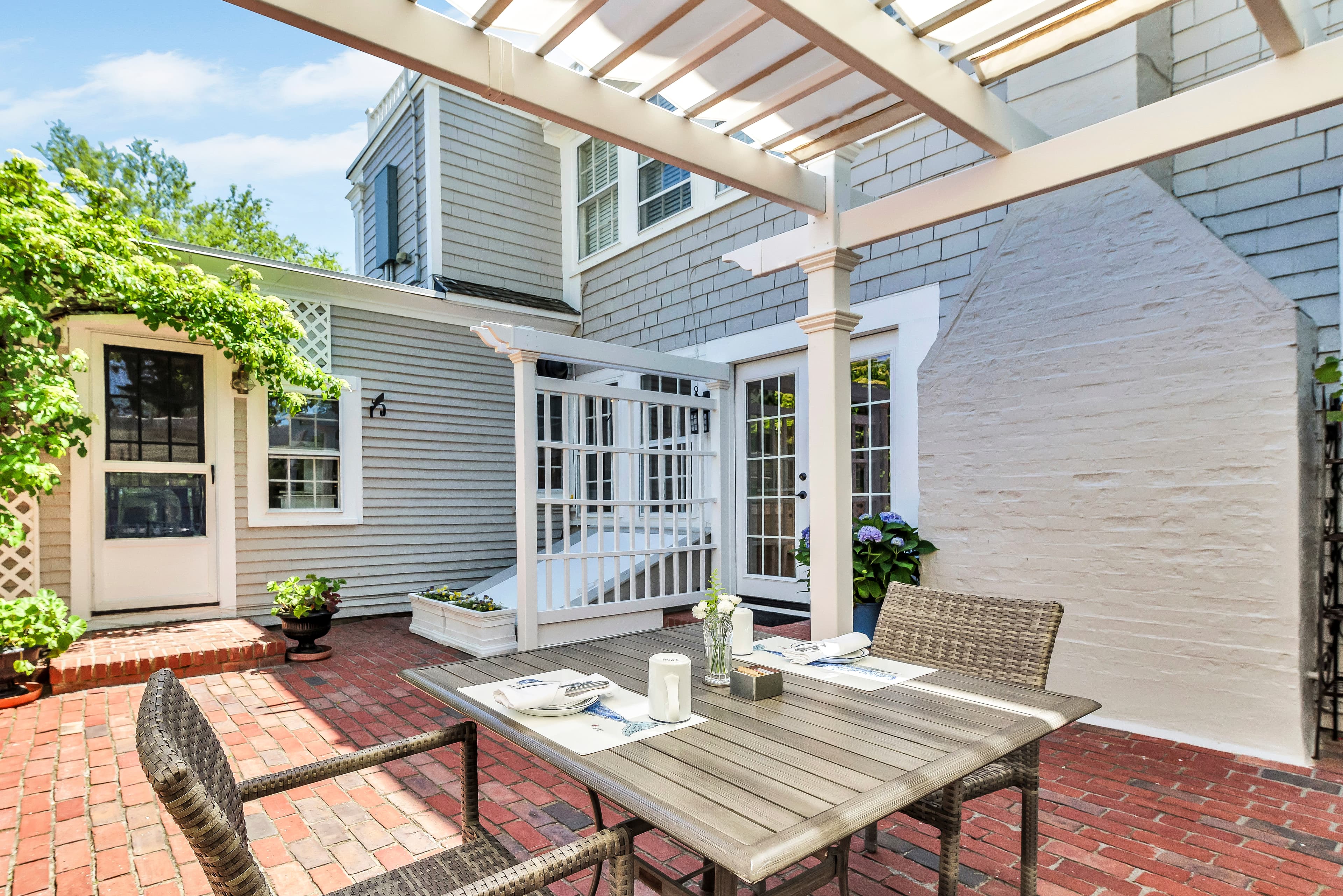 An inviting outdoor patio with a dining table, surrounded by greenery and casual seating.
