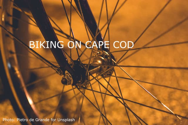 Close-up of a bicycle wheel at night with the text "Biking on Cape Cod."