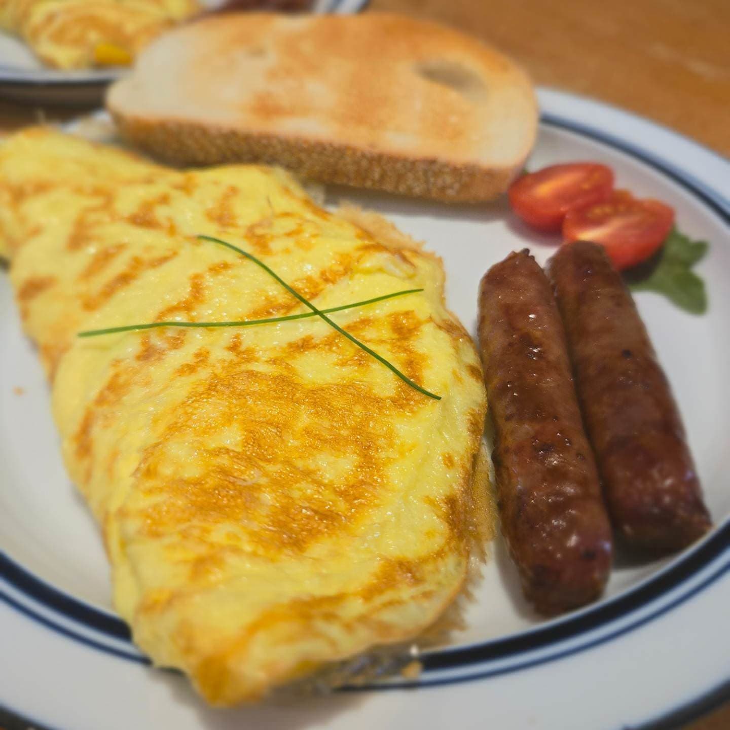 A plate of omelette garnished with chives, two sausages, toast, and sliced tomatoes.