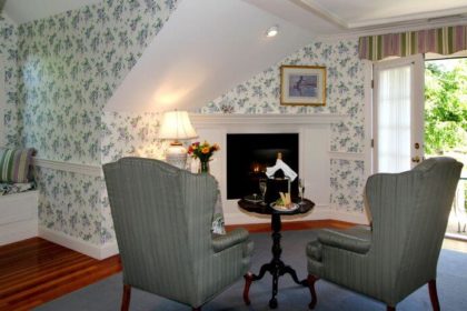 King Suite with reading nook, balcony, gas lit fireplace, green high back chairs and lavendar and green flowers on white wallpaper