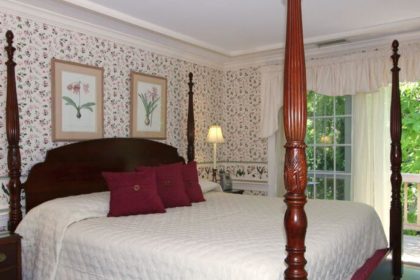 Large four-post bed made up in white in a bedroom with crown moulding and french doors.