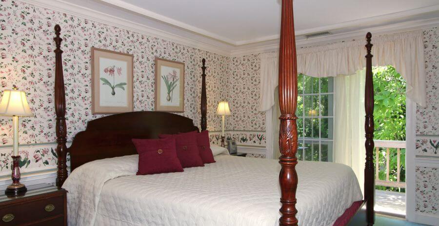 Large four-post bed made up in white in a bedroom with crown moulding and french doors.