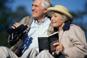 Man holding binoculars and woman holding bird book and wearing straw hat.