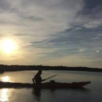 Image of a woman kayaking in the open water at sunrise.